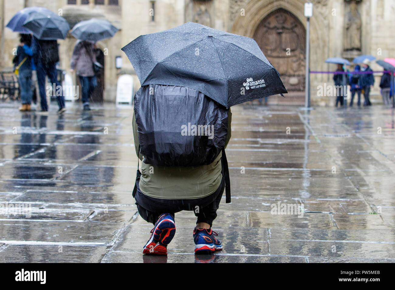 Bath, UK. 12th October, 2018. A man is pictured a he takes a photograph in front of Bath Abbey as heavy rain showers make their way across the UK. Credit: Lynchpics/Alamy Live News Stock Photo