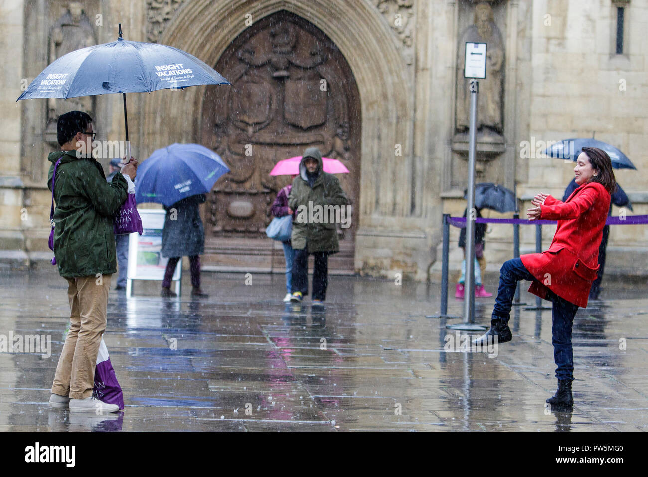 Bath, UK. 12th October, 2018. Tourists are pictured as they take a photograph outside Bath Abbey as heavy rain showers make their way across the UK. Credit: Lynchpics/Alamy Live News Stock Photo