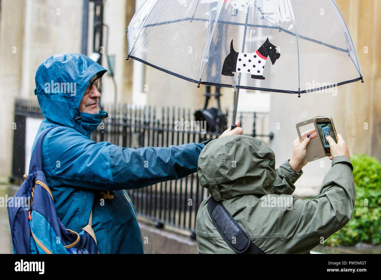 Bath, UK. 12th October, 2018. Tourists are pictured as they take a photograph outside the Pump Rooms as heavy rain showers make their way across the UK. Credit: Lynchpics/Alamy Live News Stock Photo