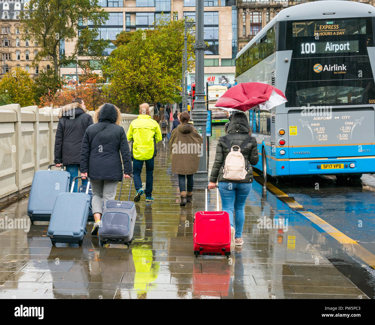 Waverley Bridge, Edinburgh, Scotland, United Kingdom, 12th October 2018. UK Weather: Rain heralds the arrival of Storm Callum in the capital city, but doesn't deter the tourists. The wind breaks a woman's umbrella. Tourists walk in the rain with wheeled suitcases to the airport 100 bus service Stock Photo