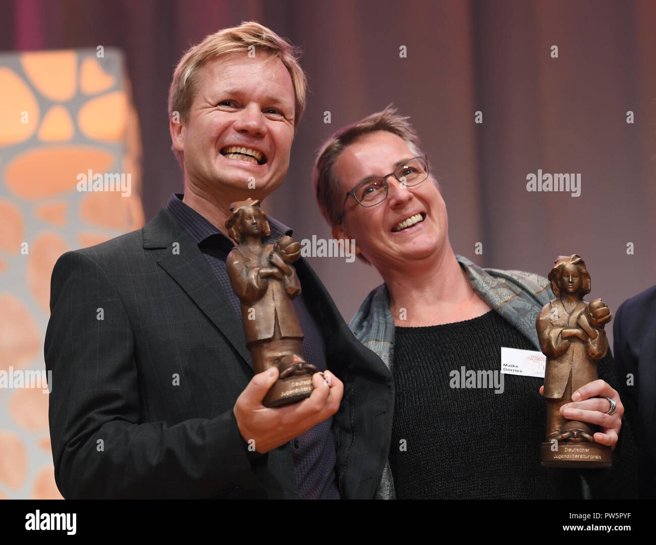 12 October 2018, Hessen, Frankfurt/Main: 12 October 2018, Germany, Frankfurt am Main: Author and illustrator Oyvind Torseter from Norway and translator Maike Doerries holding the Momo trophies at the Frankfurt Book Fair during the 2018 German Youth Literature Award ceremony. They received the award in the category 'Picture Book' for their book 'The Seventh Brother'. Photo: Arne Dedert/dpa Stock Photo