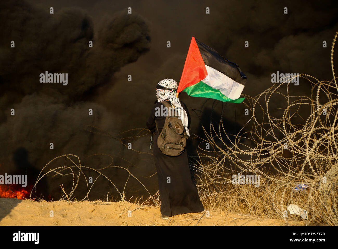 October 12, 2018 - Palestinian protesters clash with Israeli troops along the Gaza-Israeli border on the east of Khan Yunis, in the southern Gaza Strip, on 12 November 2018. According the Gaza Health Ministry six Palestinians have been killed by Israeli live fire and over two hundred wounded by Israeli live ammunition and tear gas during this Friday protest along the Gaza border with Israel. Thousands of Palestinians attended the March of Return rally and some burnt tyres and threw stones towards the fence and the Israeli soldiers positioned on the other side. According to Israeli milita Stock Photo