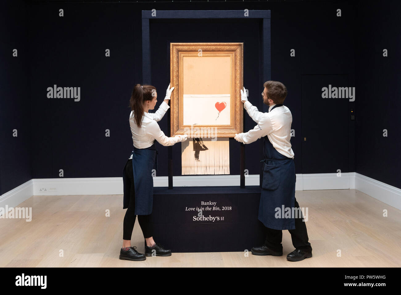 London, UK. 12th Oct, 2018. Sotheby's staff members present Banksy's 'Love is in the Bin' in London, Britain on Oct. 12, 2018. Originally titled 'Girl with Balloon', the British street artist Banksy made his painting self-destruct on Oct. 5 moments after it was auctioned for 1.042 million British pounds (1.37 million U.S. dollars) at Sotheby's in London. Credit: Ray Tang/Xinhua/Alamy Live News Stock Photo