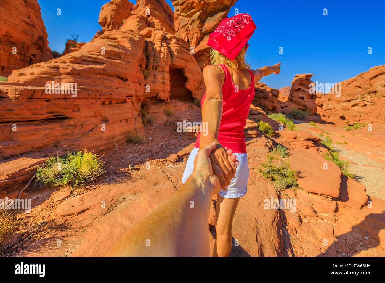 Follow me, young sporty girl holding hands at Firecave, the rock formations in Valley of Fire State Park, Nevada, USA. Concept of the journey. Tourist traveler holding man by hand. Stock Photo