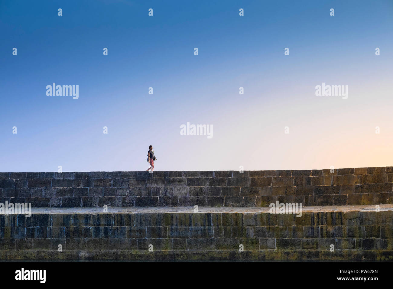 A woman walking along the top of The Cobb in the coastal town of Lyme Regis in Dorset. Stock Photo