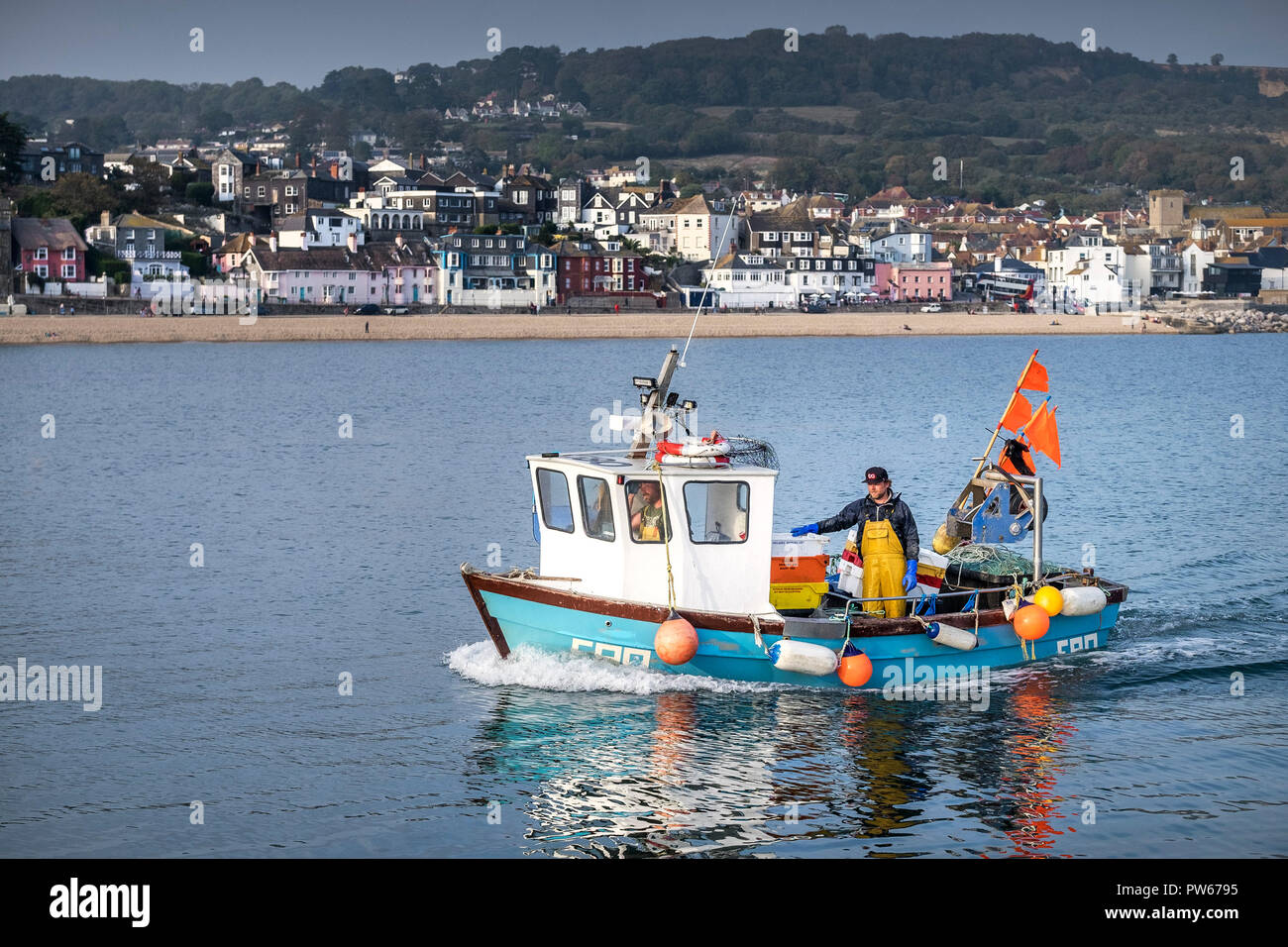 A small fishing boat steaming sailing past the coastal town of Lyme Regis in Dorset. Stock Photo