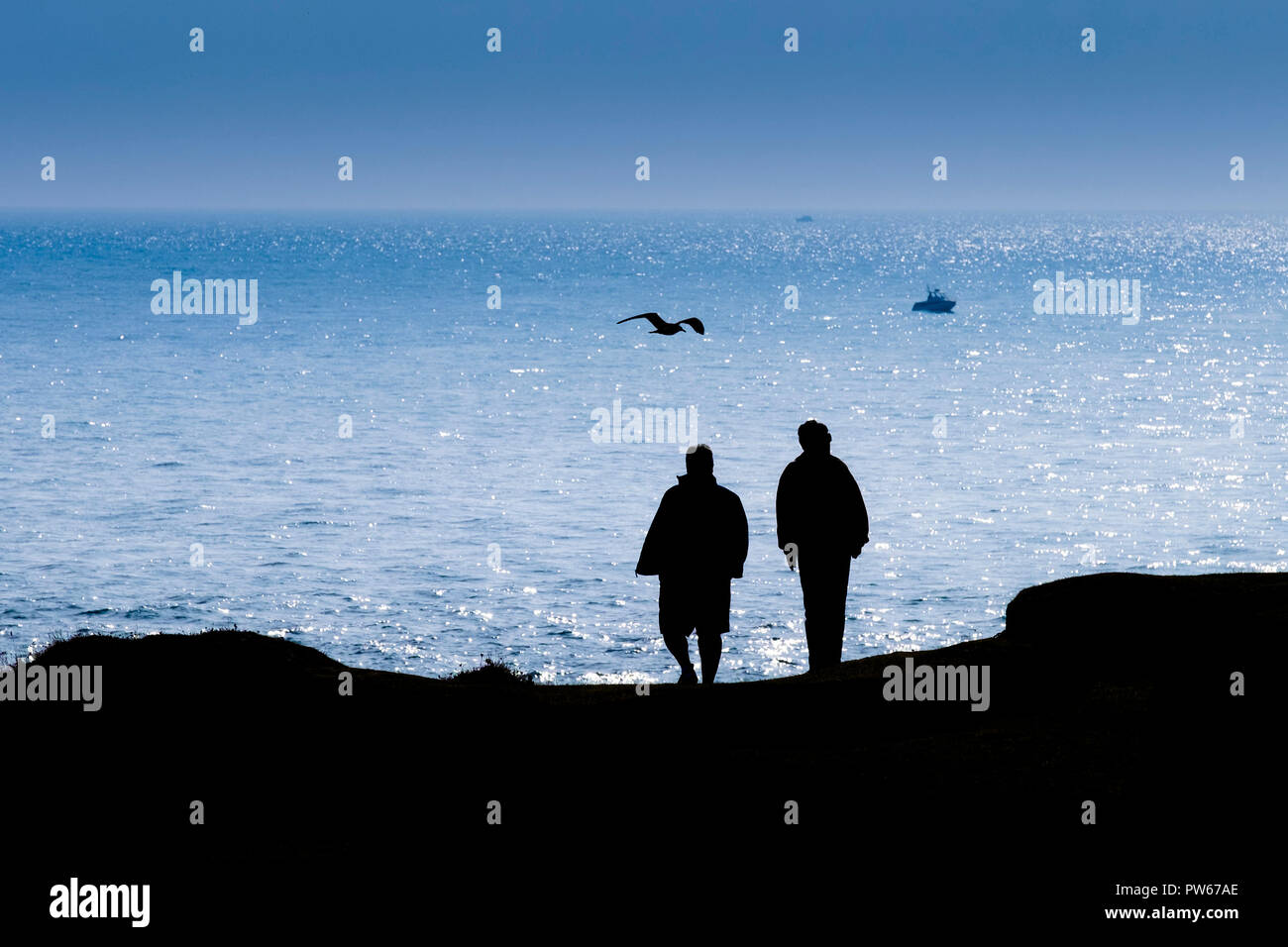 Two people seen in silhouette standing on Portland Bill overlooking the sea. Stock Photo