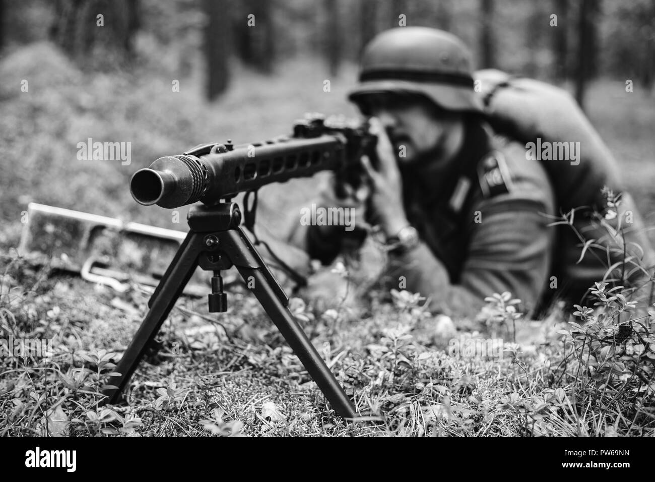 Hidden Unidentified Re-enactor Dressed As German Wehrmacht Soldier Aiming A Machine Gun At Enemy From Trench In Forest. Photo In Black And White Color Stock Photo