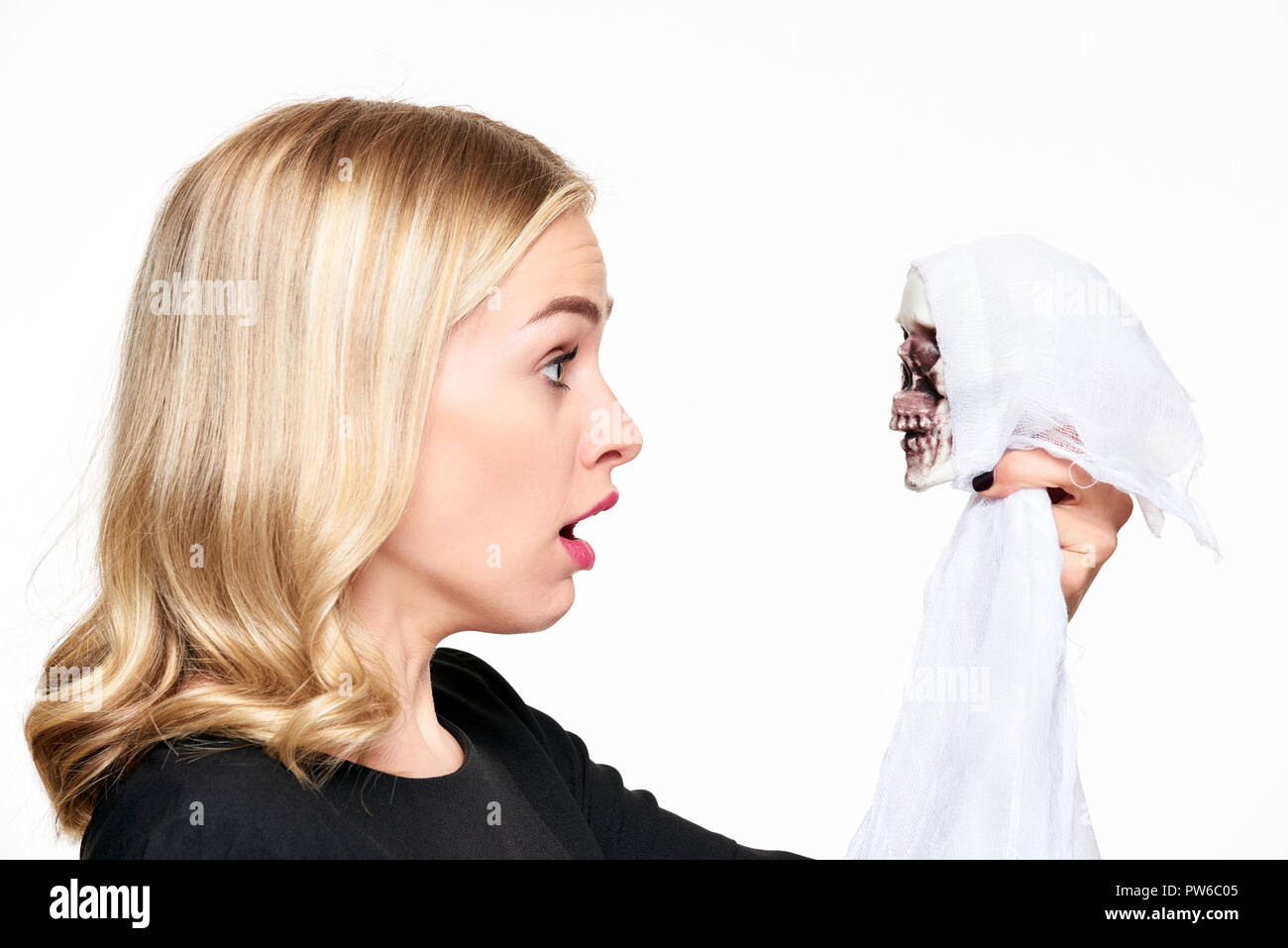 Shocked young woman face to face with Halloween skeleton death decoration. Halloween concept over white background. Stock Photo