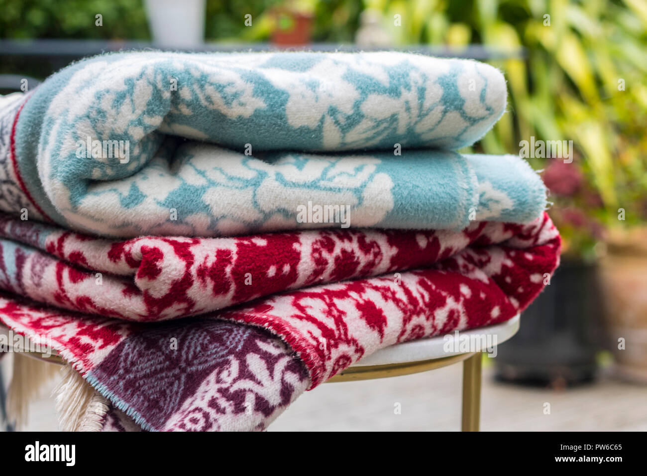 Pile of blankets on a table in the garden, summer evenings concept, warm warmth, cream fringe picnic, outdoor al fresco concept hygge relax relaxing Stock Photo
