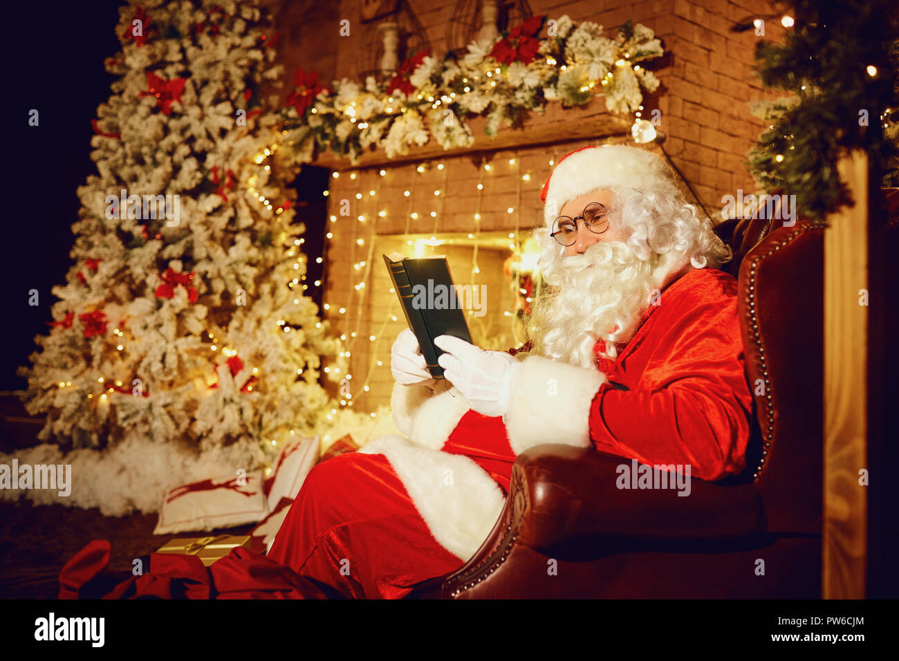 Santa Claus is reading a book in a room with a fireplace in Chri Stock Photo