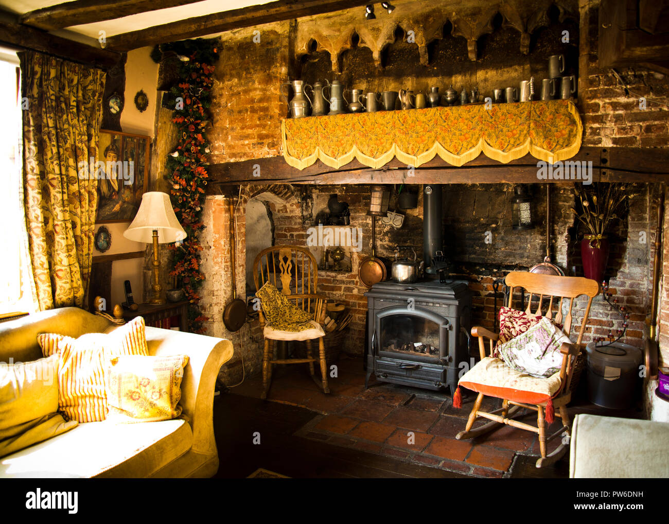 Old fireplace in the drawing room of an old country village house surrounded with decorative antique furniture and interesting objects hanging on wall Stock Photo