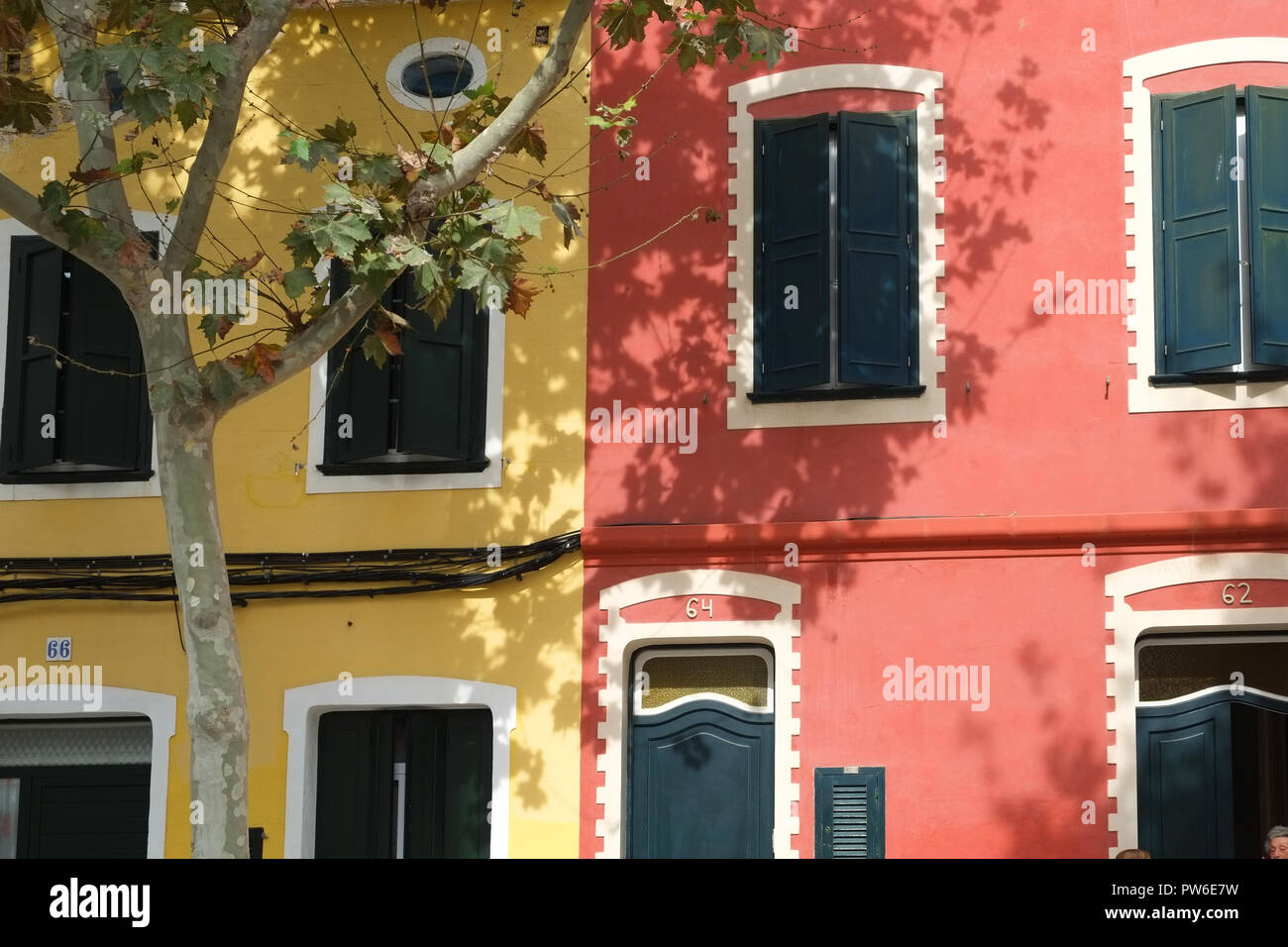 Shadows of trees fall across the colourful terraced houses and shutters in Carrer Victori, Es Castell, Menorca, Spain Stock Photo