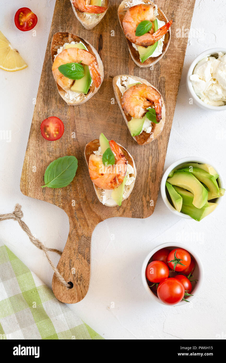 Bruschetta italian snack sandwiches with shrimps, avocado and cheese decorated by basil. Stock Photo