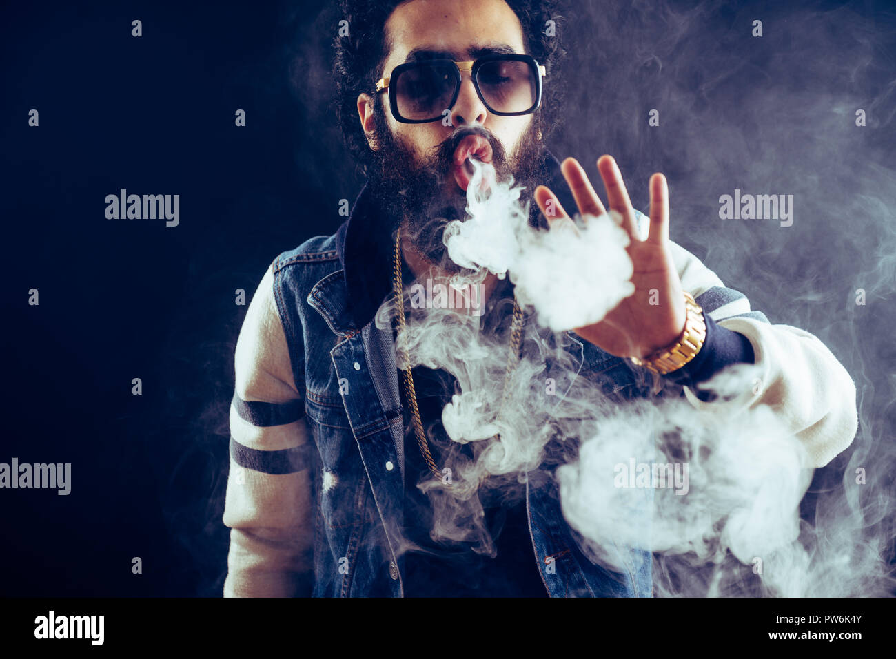 Smoking vape. vaping man holding a mod. Vape Rings. A man launches a ring of smoke. Tricks with smoke. Stock Photo