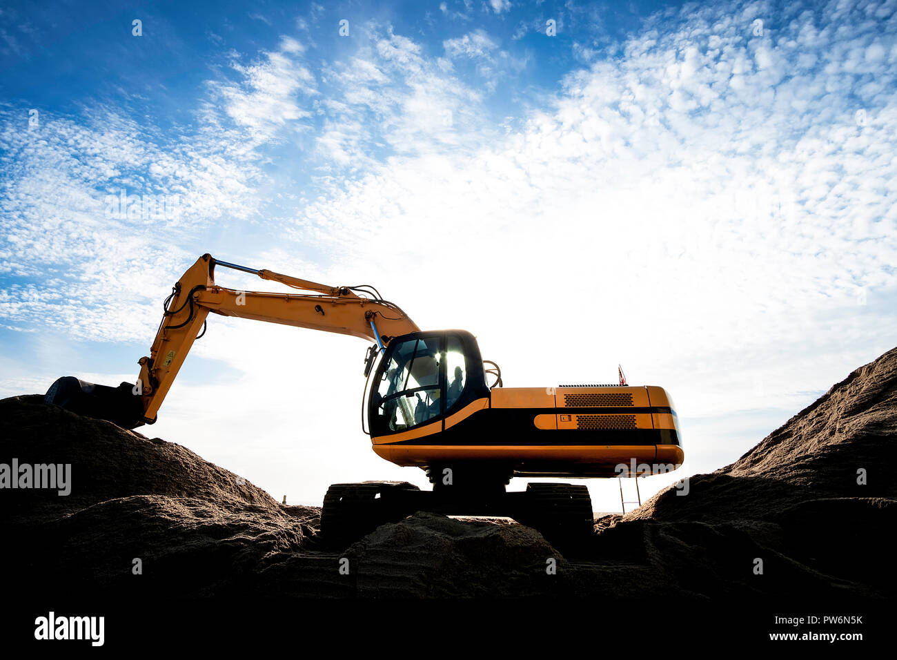 yellow excavating machine over sand dunes, against partly cloudy sky. Stock Photo
