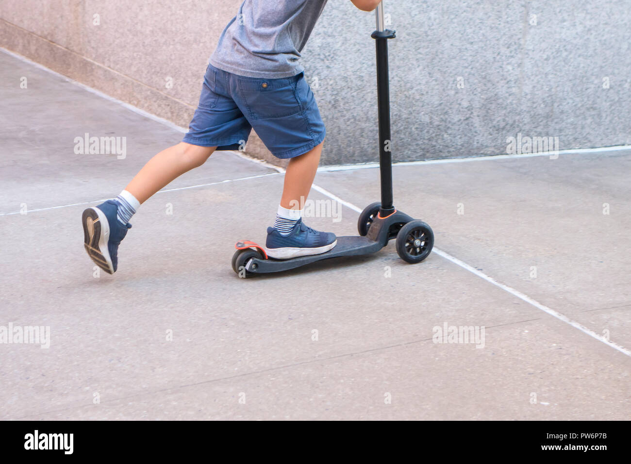 Boy on a plastic 3 wheel mini scooter on a urban sidewalk Stock Photo
