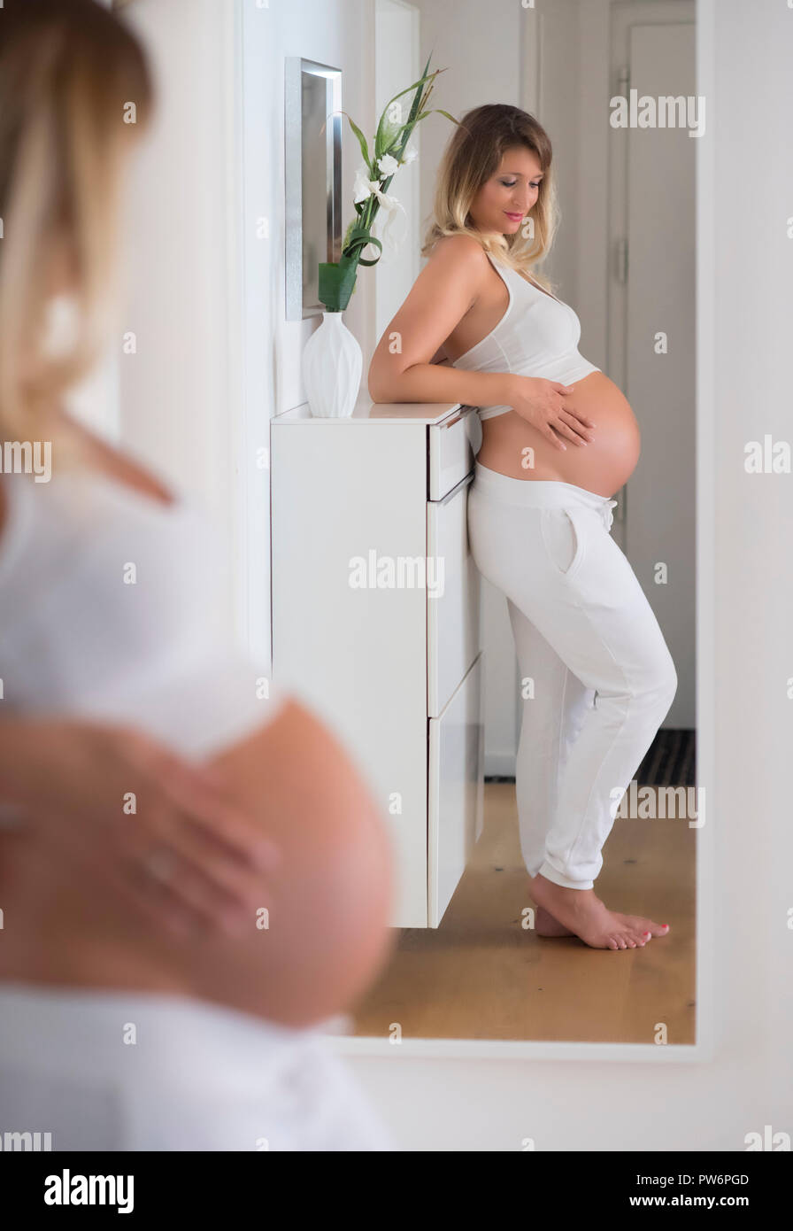 Woman in her ninth month pregnant, looks at herself in the mirror, Germany Stock Photo