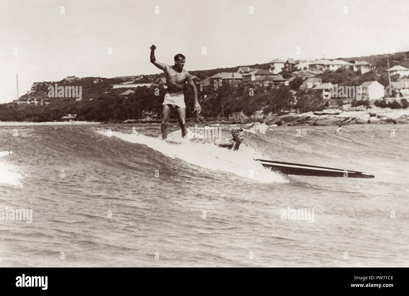 Man and woman surfing tandem on a longboard in 1945 at Manly Beach, Sydney, Australia. (Photo by Ray Leighton) Stock Photo