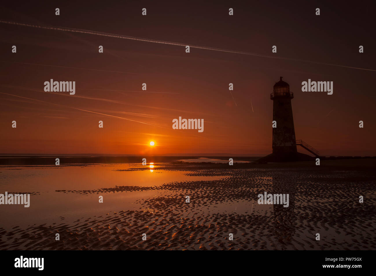Point of Ayr lighthouse on Talacre beach at sunrise reflecting in a tidal pool, North Wales coast Stock Photo