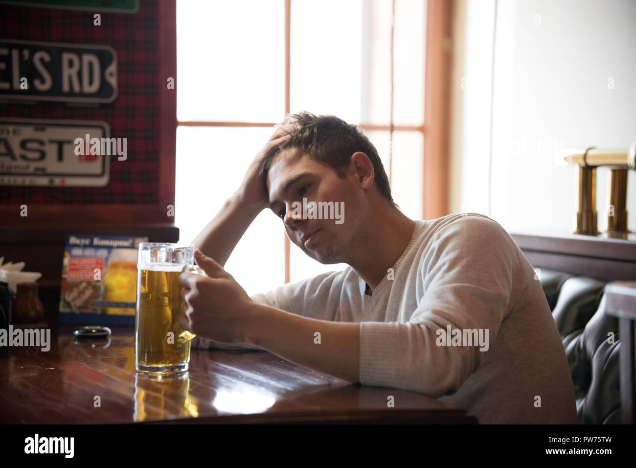 Stressed young man drinks beer in the pub. The man holds the glass ...