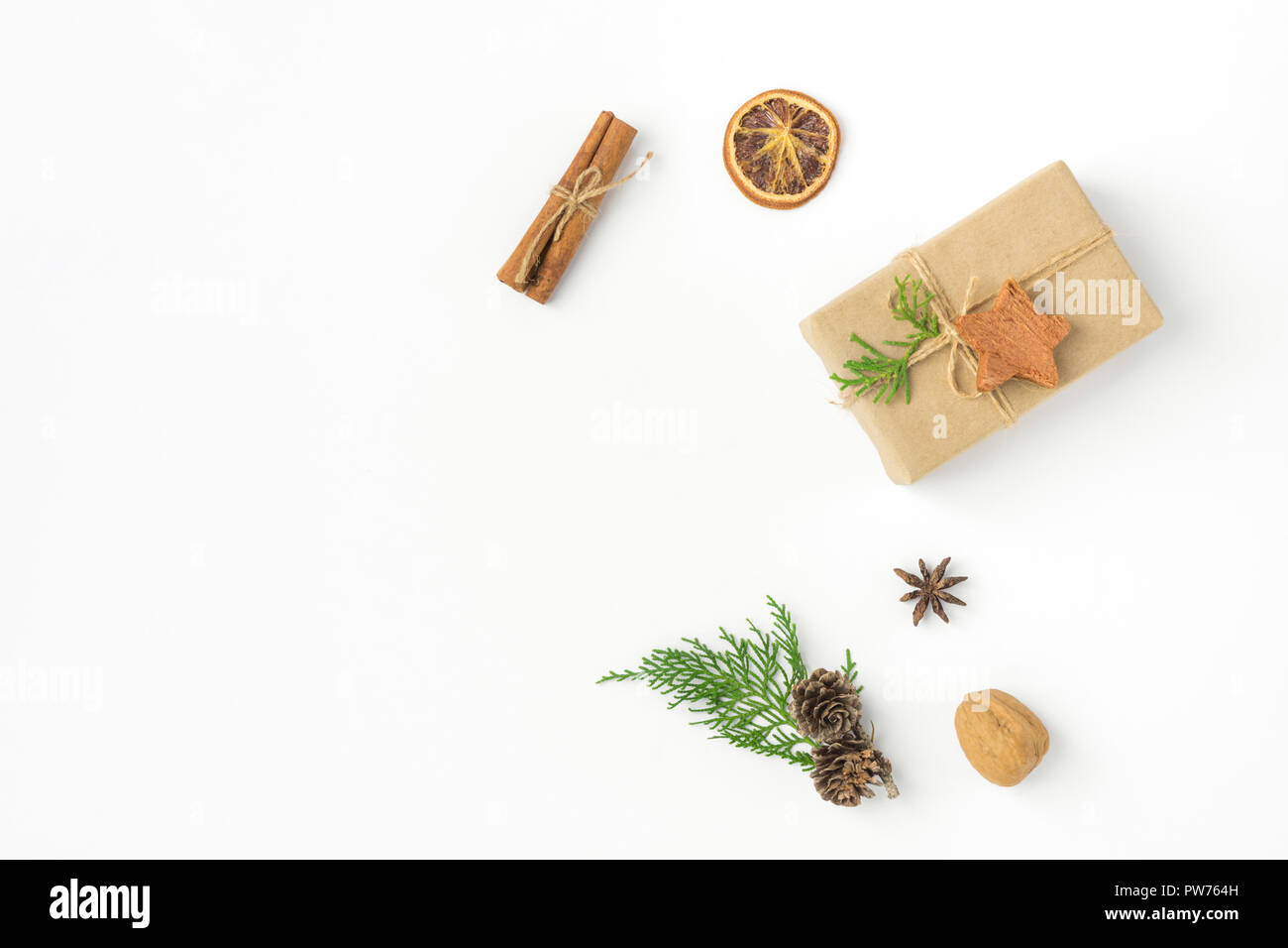 Gift box wrapped in craft paper tied with twine pine cones juniper nuts cinnamon on solid white background. New Year presents holiday preparations DIY Stock Photo