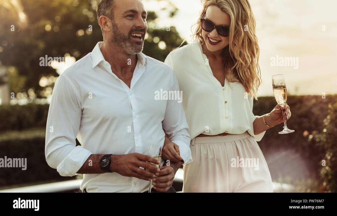 Cheerful man and woman with a drink outdoors. Wealthy couple together with a glass of wine. Stock Photo