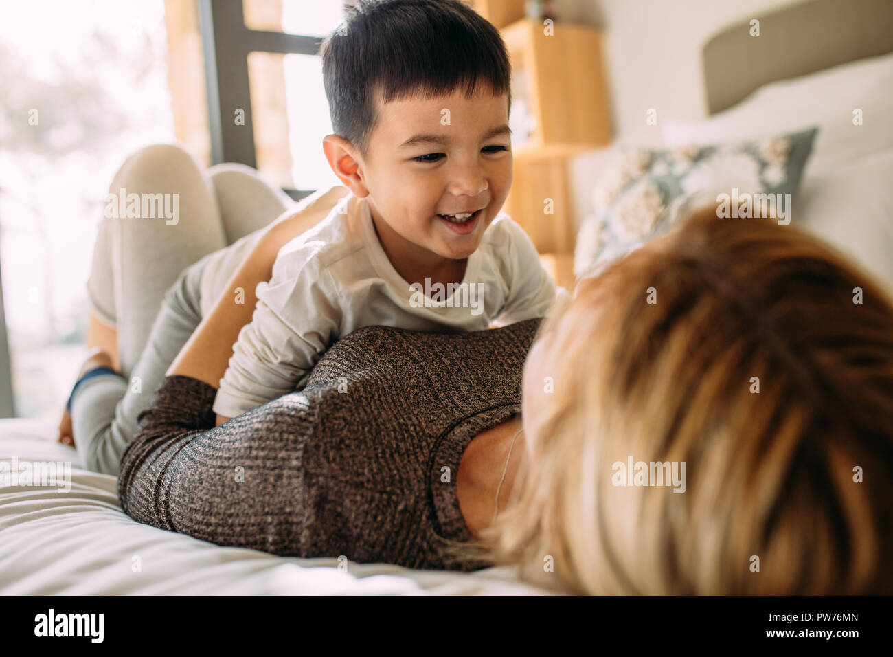 Cute little kid playing with his mother on bed. Mother and son having a fun time at home. Stock Photo