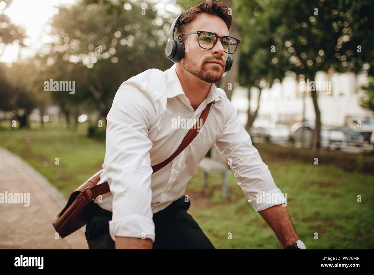 Man commuting to office on a bicycle early in the morning. Man wearing office bag and wireless earphones riding a bicycle. Stock Photo