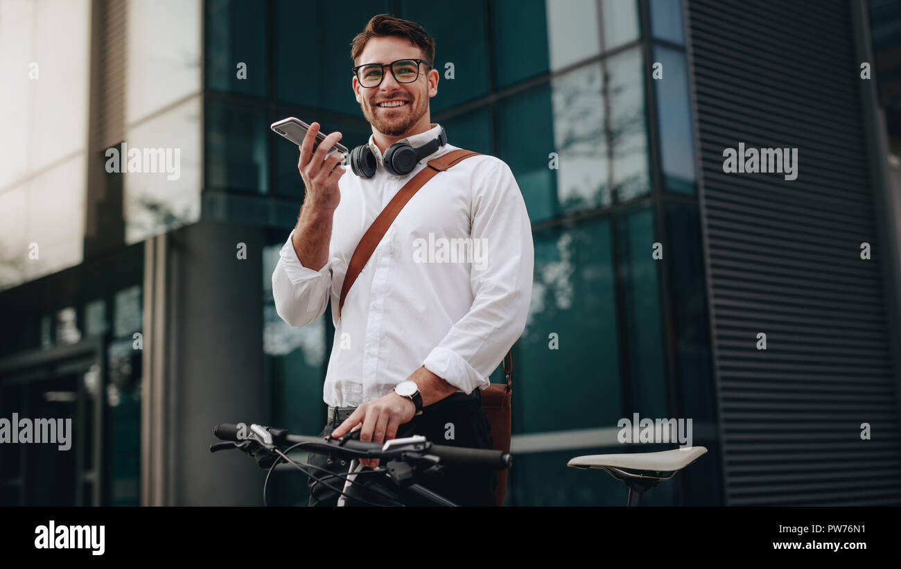 Smiling businessman talking over mobile phone standing on street with his bicycle. Man stopping by to make a call and while commuting to office on a b Stock Photo