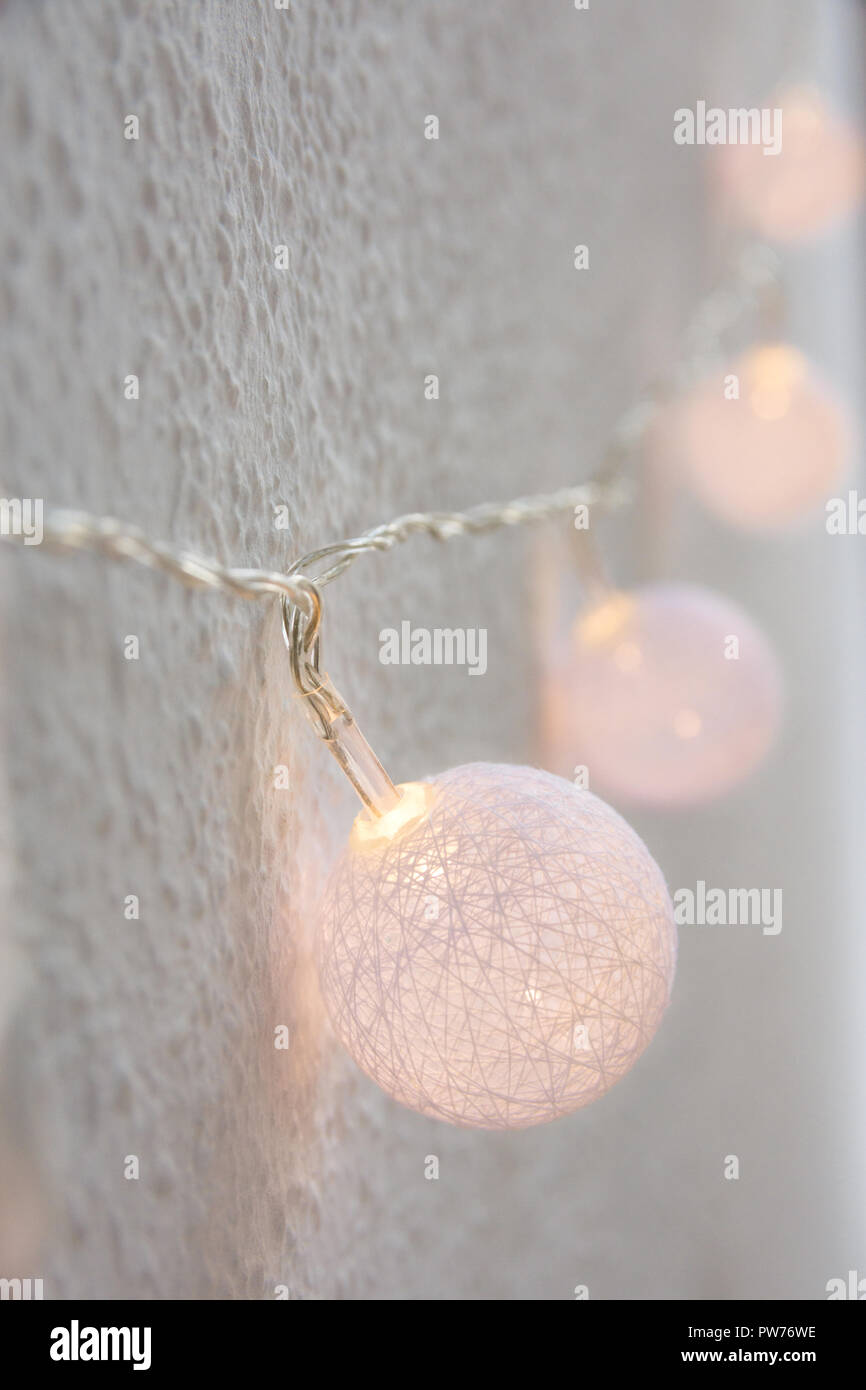 Christmas New Year Background. Hanging Pastel Golden Cotton Balls Garland White Wall Background. Scandinavian Style. Glittering Lights. Cozy Festive A Stock Photo