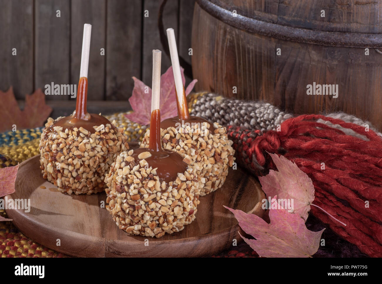 Taffy apples coated with nuts on a wooden plate in a rustic setting Stock Photo