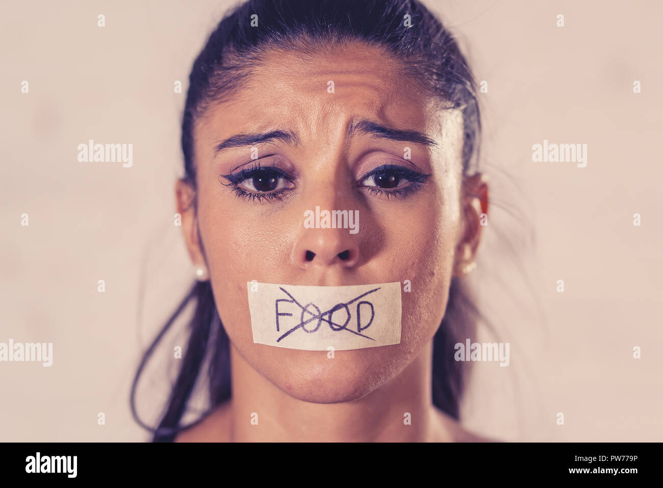 Close up portrait of young attractive latin woman with mouth sealed on stick tape with text no food in diet Anorexia eating disorder concept. Stock Photo