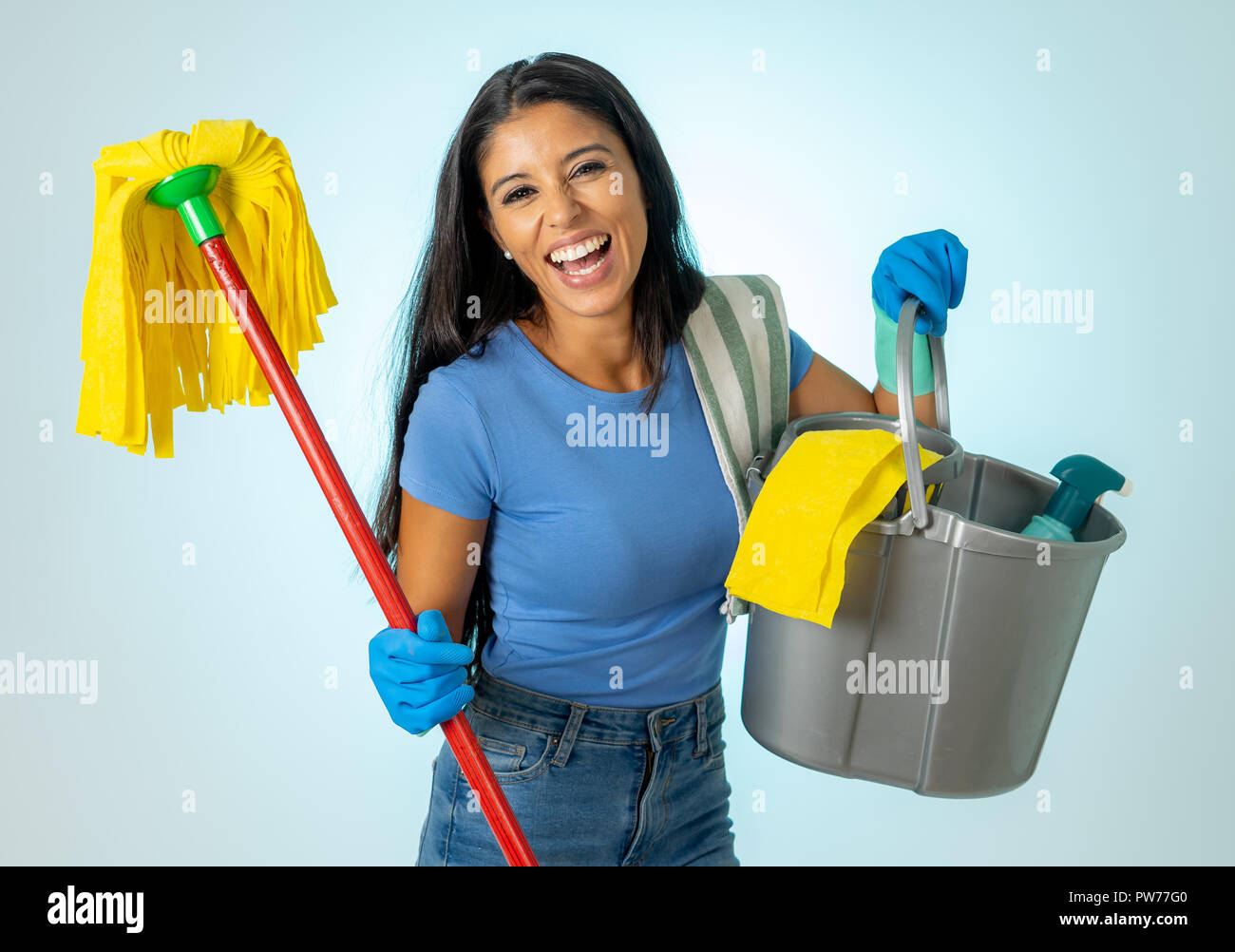 Beautiful happy latin woman holding cleaning equipment in Cleaning service Professional, housemaid and housework isolated on blue background. Stock Photo