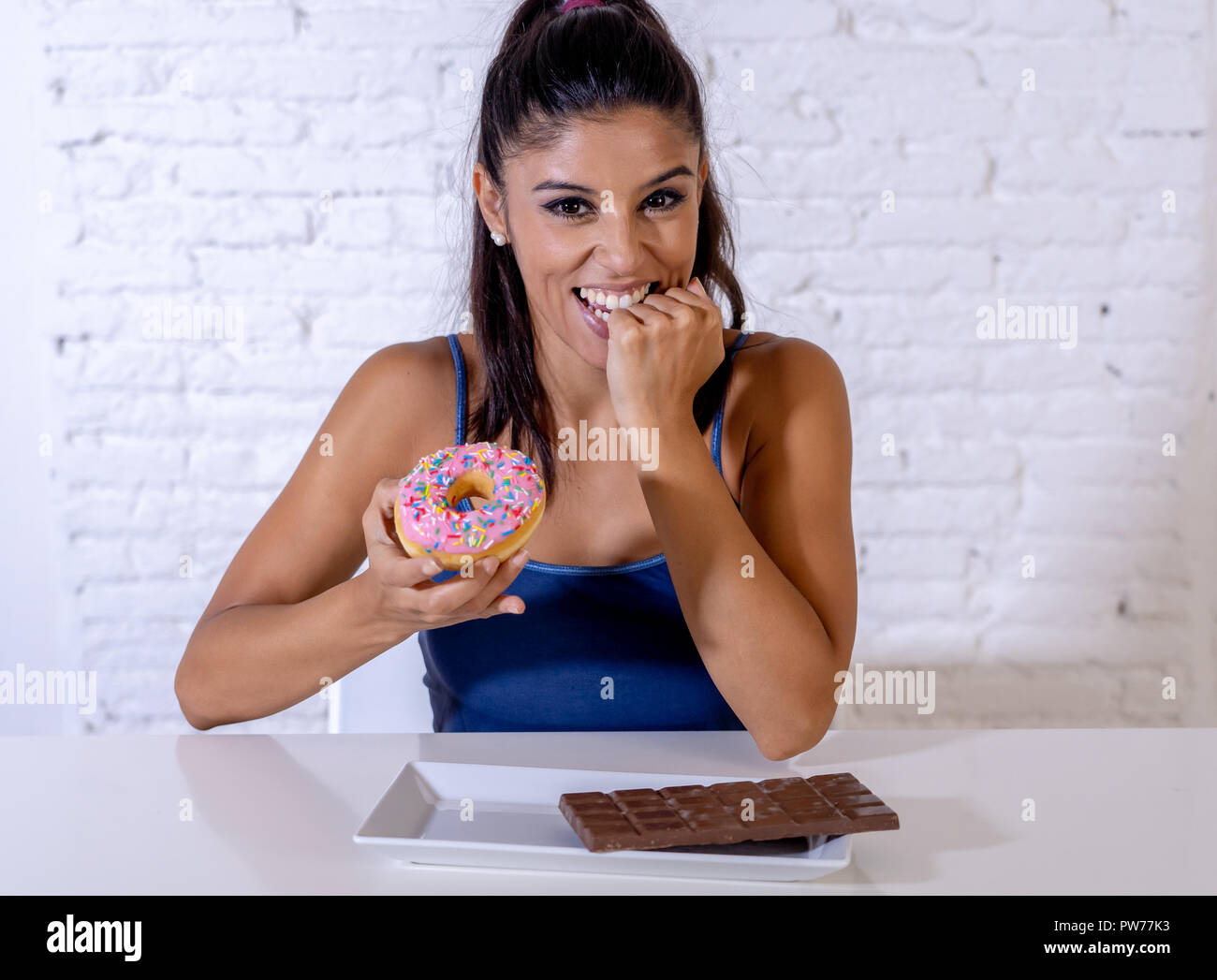 Young attractive latin woman sitting at table about to eat chocolate and doughnuts looking excited and happy in no more diet, sugar and chunky unhealt Stock Photo