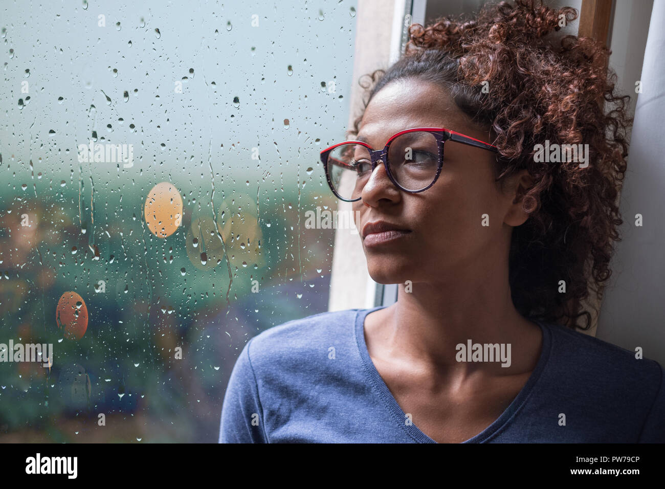Sad african american girl looking out of the window on rainy weather Stock Photo