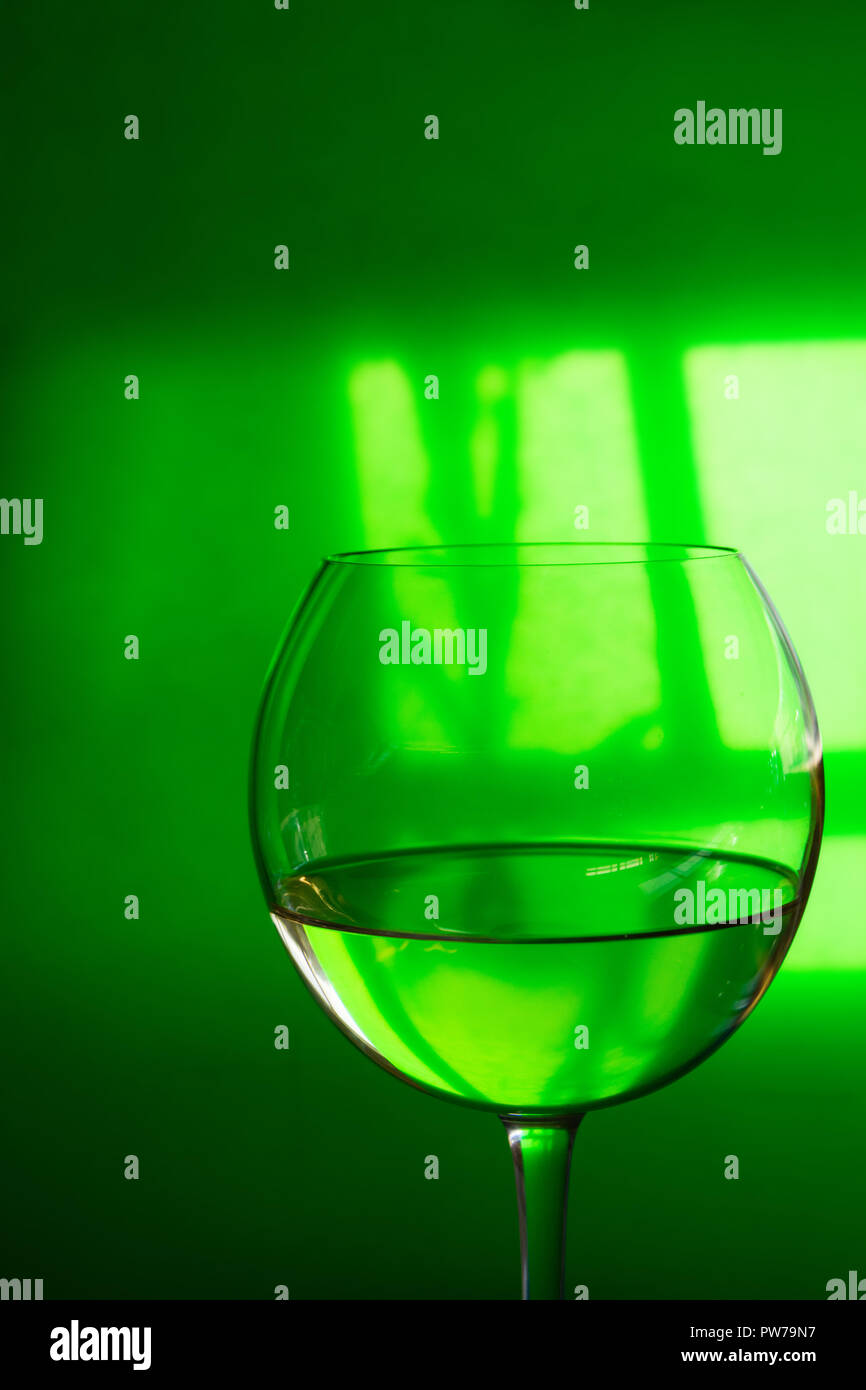Glass of transparent white dry wine on green translucent background with window reflexion hard shadows. Conceptual creative minimalist image. Indulgen Stock Photo