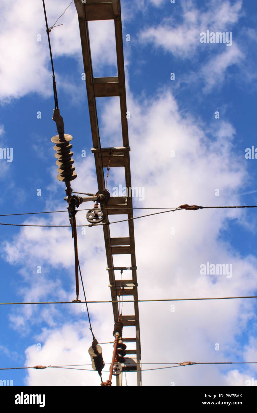 Train Travel - Overhead signal cables and railway infrastructure set against blue sky with white clouds Stock Photo