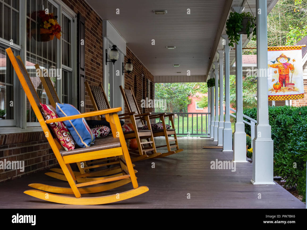 Rocking chairs lined up on long front porch. Red barn is in the background. Stock Photo