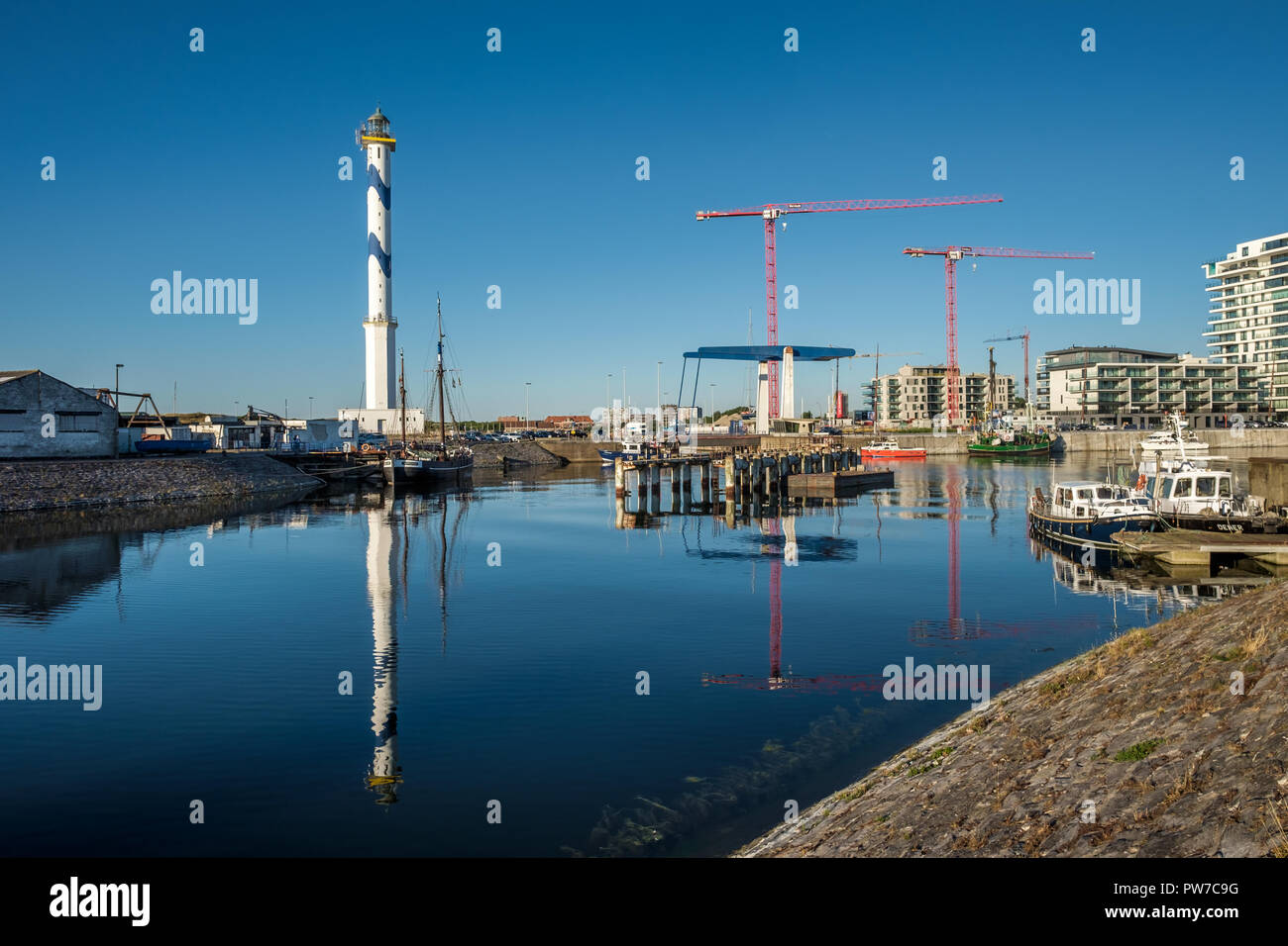 Old lighthouse of Ostend known as ‘Lange Nelle’, reflected in a commercial dock, Thursday 2 August 2018, Oostende, Belgium Stock Photo