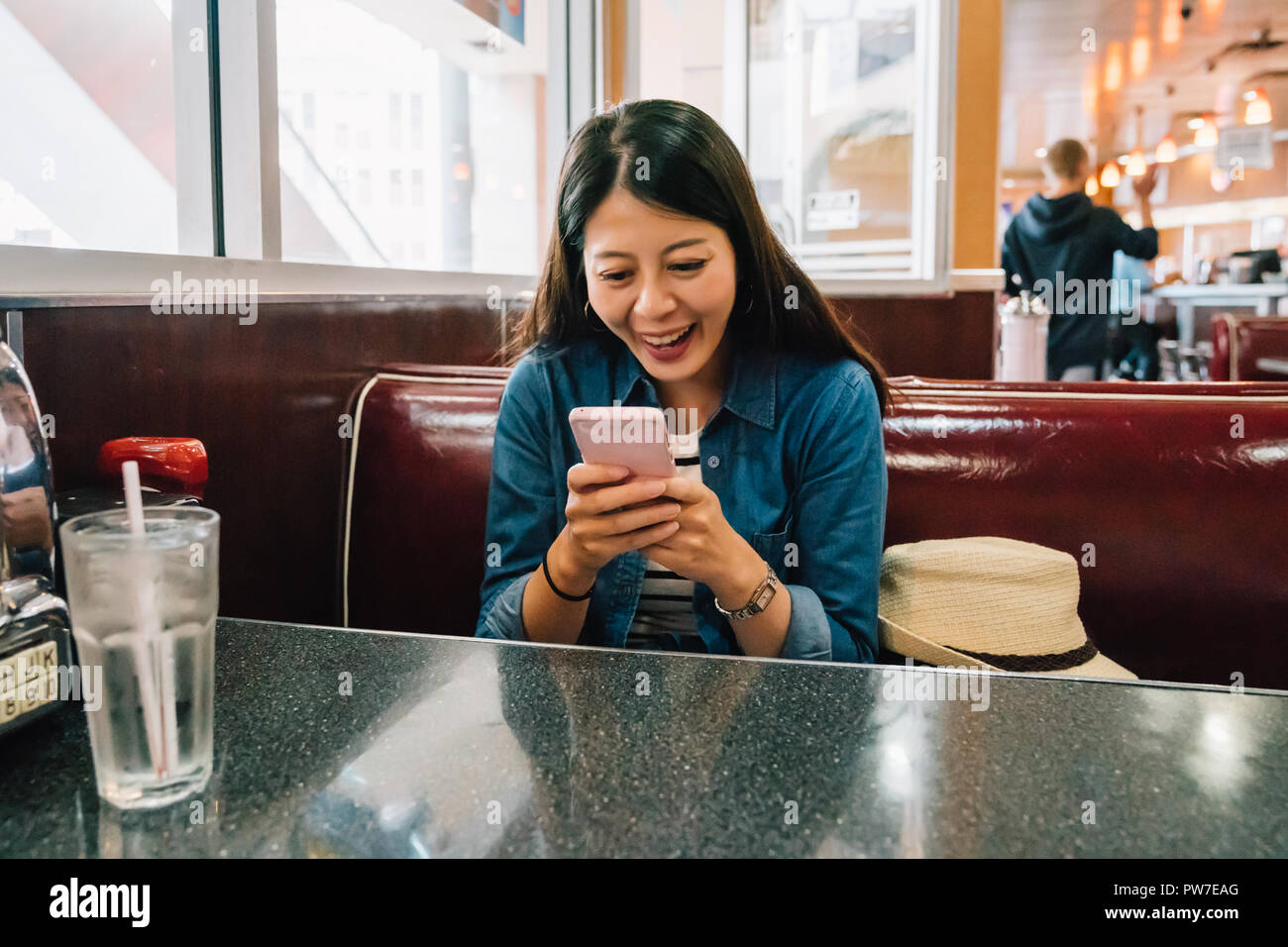 casual lady relaxing sitting in the diner and joyfully chatting with her friend by smartphone while waiting the meal. young woman joyfully using mobil Stock Photo