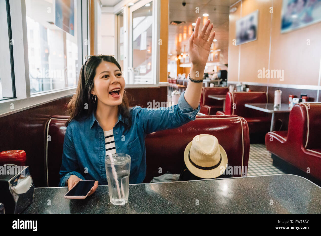 hungry lady cheerfully calling waiter to order food, because she finally find a restaurant to eat, young girl happy to see her friends show up and say Stock Photo