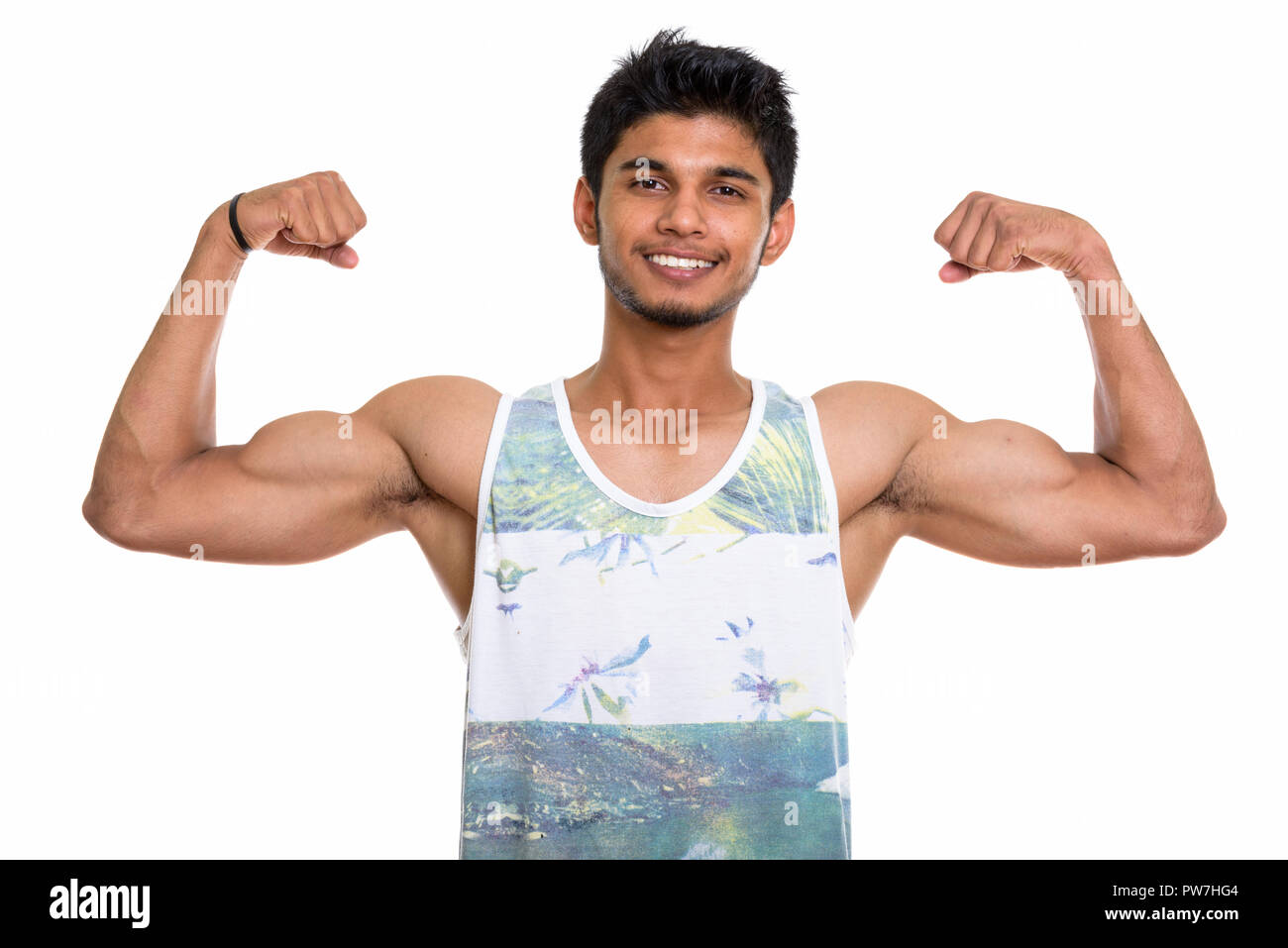 Studio shot of young happy Indian man smiling while flexing both Stock Photo