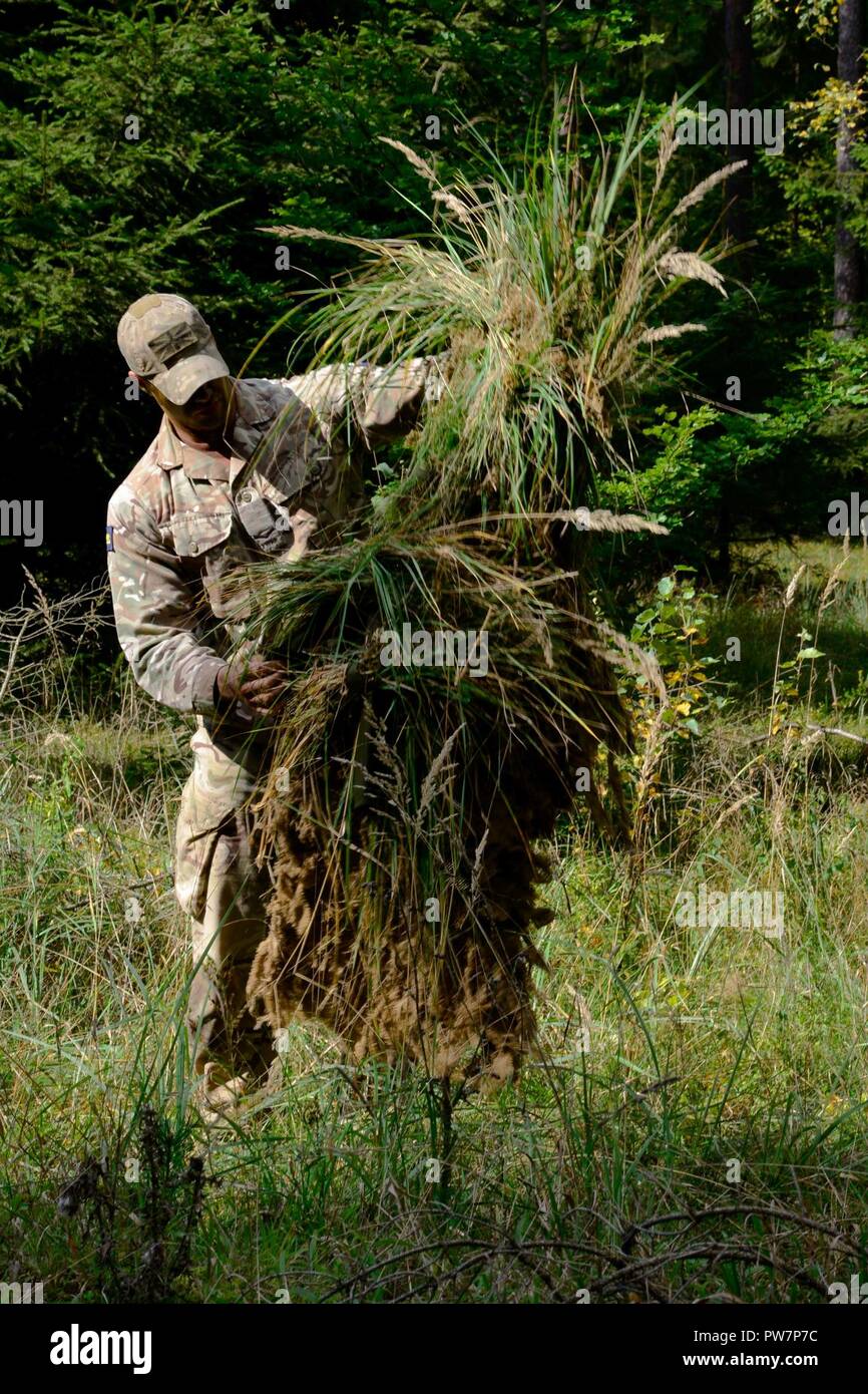 A British soldier prepares his ghillie suit during the European Best Sniper Squad Competition at the 7th Army Training Command Grafenwoehr Training Area, Germany, Sept. 27, 2017. The European Best Sniper Squad Competition is an U.S. Army Europe competition challenging militaries from across Europe to compete and enhance teamwork with Allies and partner nations. Stock Photo