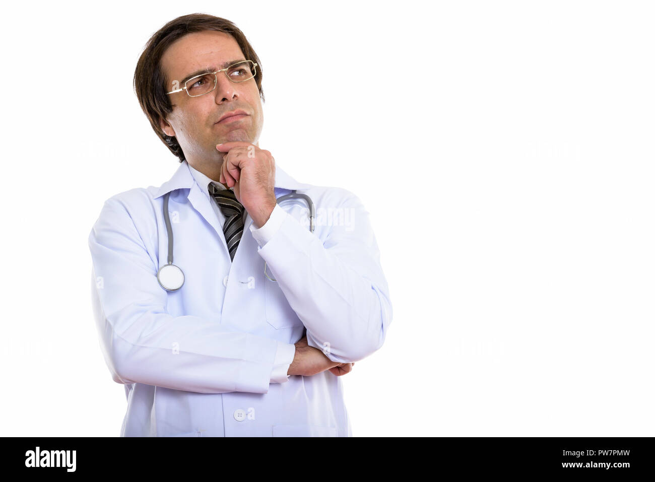 Studio shot of young Persian man doctor thinking while looking u Stock Photo