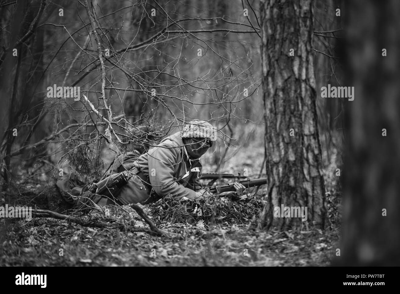 Hidden Unidentified Re-enactor Dressed As German Wehrmacht Soldier Aiming A Rifle At Enemy From Ground. Photo In Black And White Colors. Stock Photo