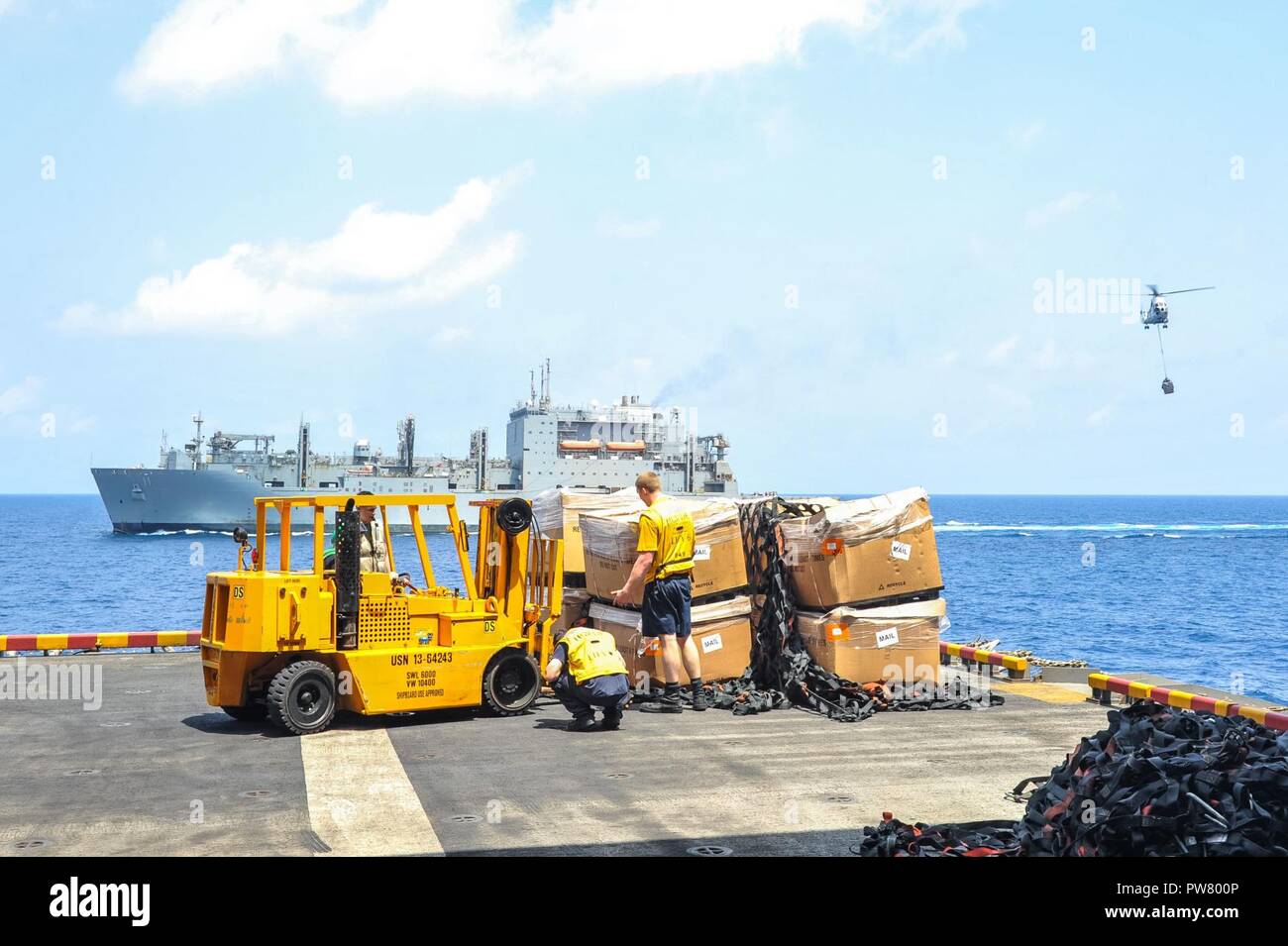 5TH FLEET AREA OF OPERATIONS (Sept. 30, 2017) Sailors aboard the amphibious assault ship USS America (LHA 6) prepare to move cargo from the starboard elevator during a replenishment-at-sea (RAS) with the Henry J. Kaiser-class underway replenishment oiler  USNS Patuxent (T-AO 201). America is the flagship for the America Amphibious Ready Group and, with the embarked 15th Marine Expeditionary Unit, is deployed to the U.S. 5th Fleet area of operations in support of maritime security operations to reassure allies and partners and preserve the freedom of navigation and the free flow of commerce in  Stock Photo