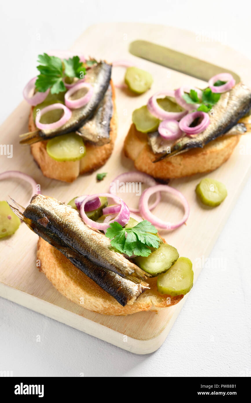 Tasty sandwiches with sprats, marinated cucumber and onion on wooden board over white  background. Stock Photo