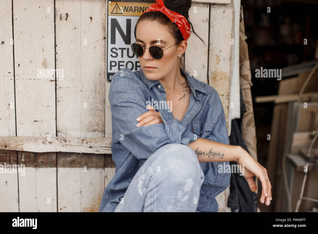 Hipster woman in denim fashionable clothes with jeans with a red bandana  and sunglasses sits near a vintage wooden timber Stock Photo - Alamy