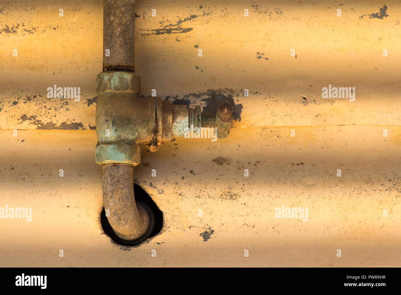 An old rusty pipe and tap running up and through a hole in a wall Stock Photo